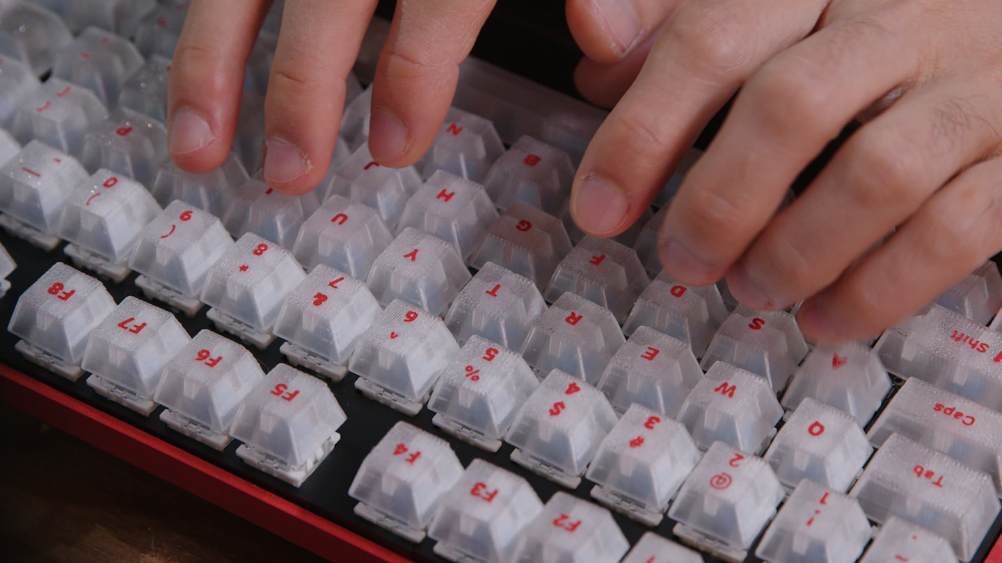 Manos escribiendo en un teclado mecánico rojo y negro con teclas blancas.