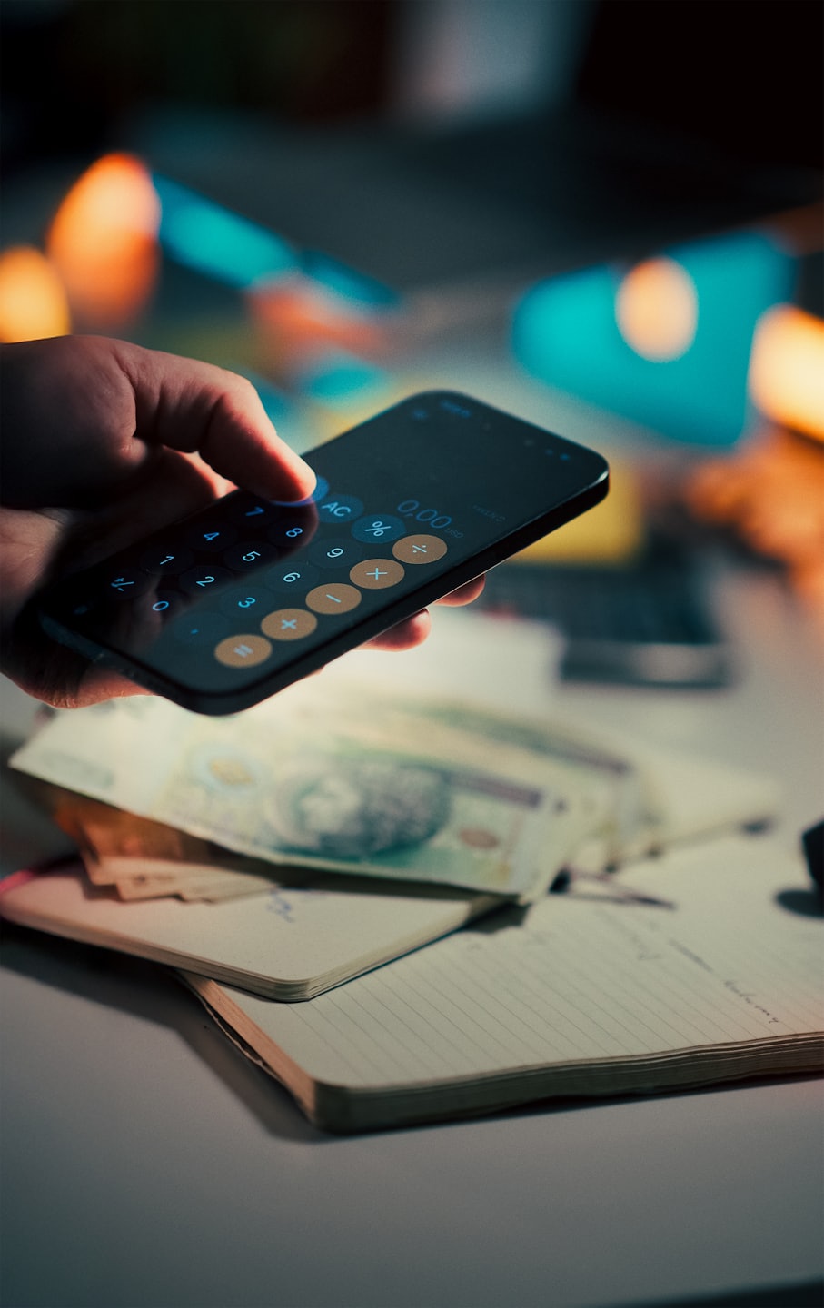 Mano usando calculadora de smartphone con dinero y cuaderno.