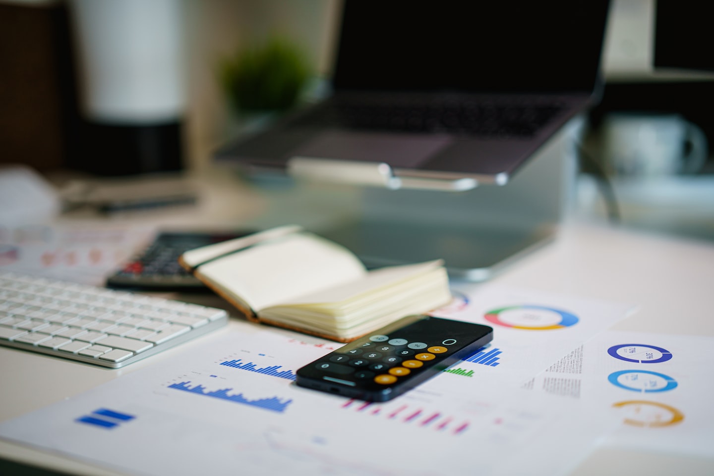 Portátil, teclado, cuaderno y smartphone sobre un escritorio con gráficos financieros.